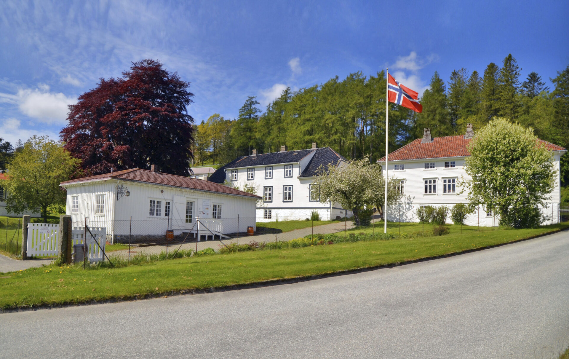 Eksteriørfoto av Dalane Folkemuseum på Slettebø på en solfylt dag med norsk flagg heist opp i museumshagen.