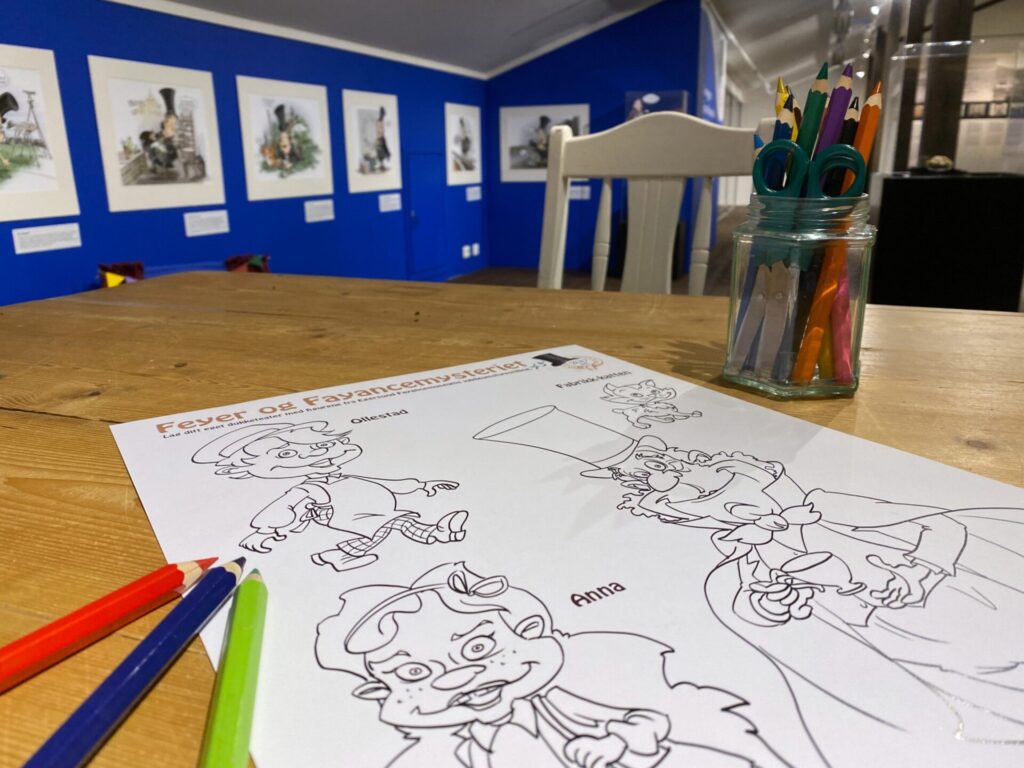 arbeidsbord for barn med fargeblyanter og fargeleggingsark med karikaturer av personer fra Feyers historie